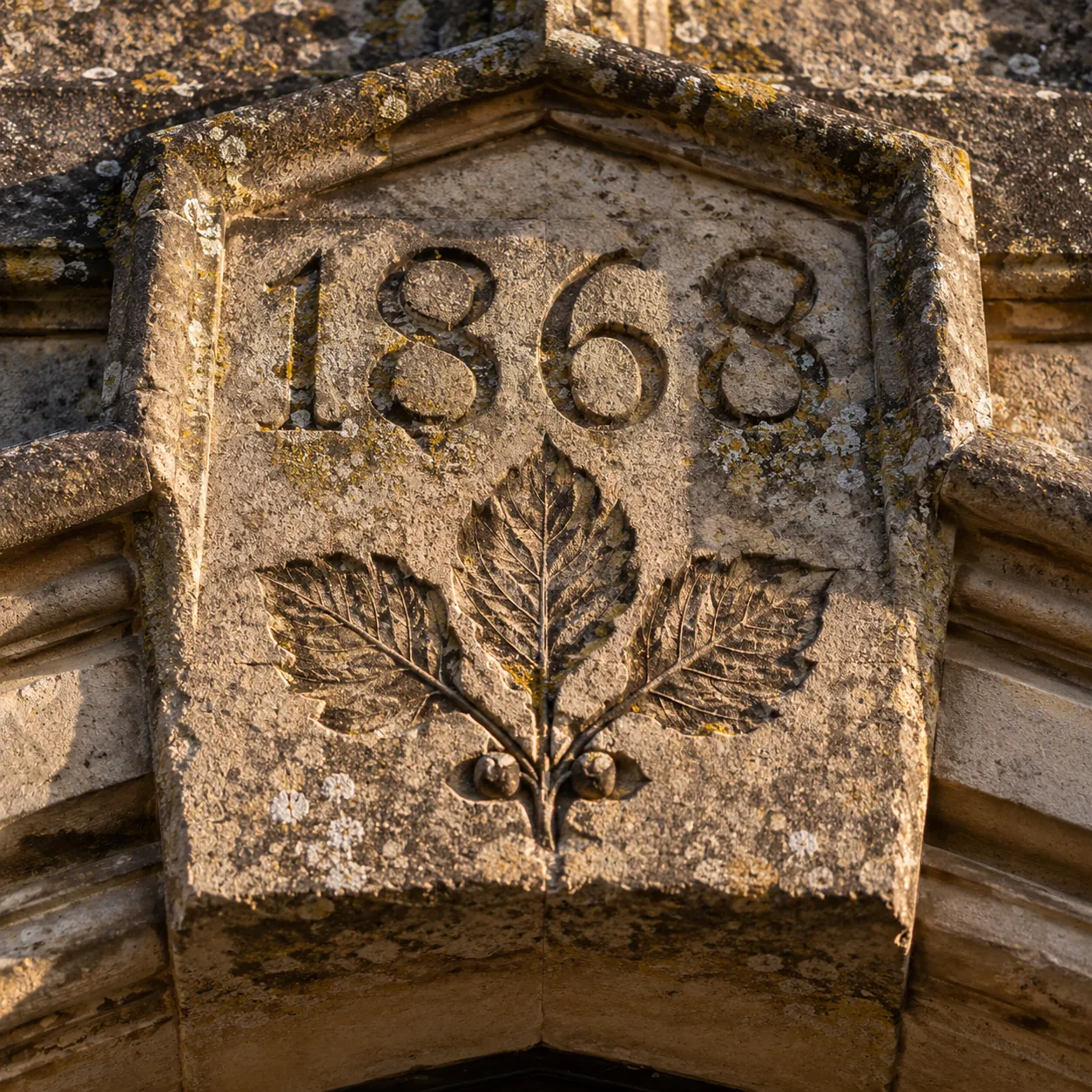 A weathered carved datestone reading 1868 with an alder leaf beneath the numerals
